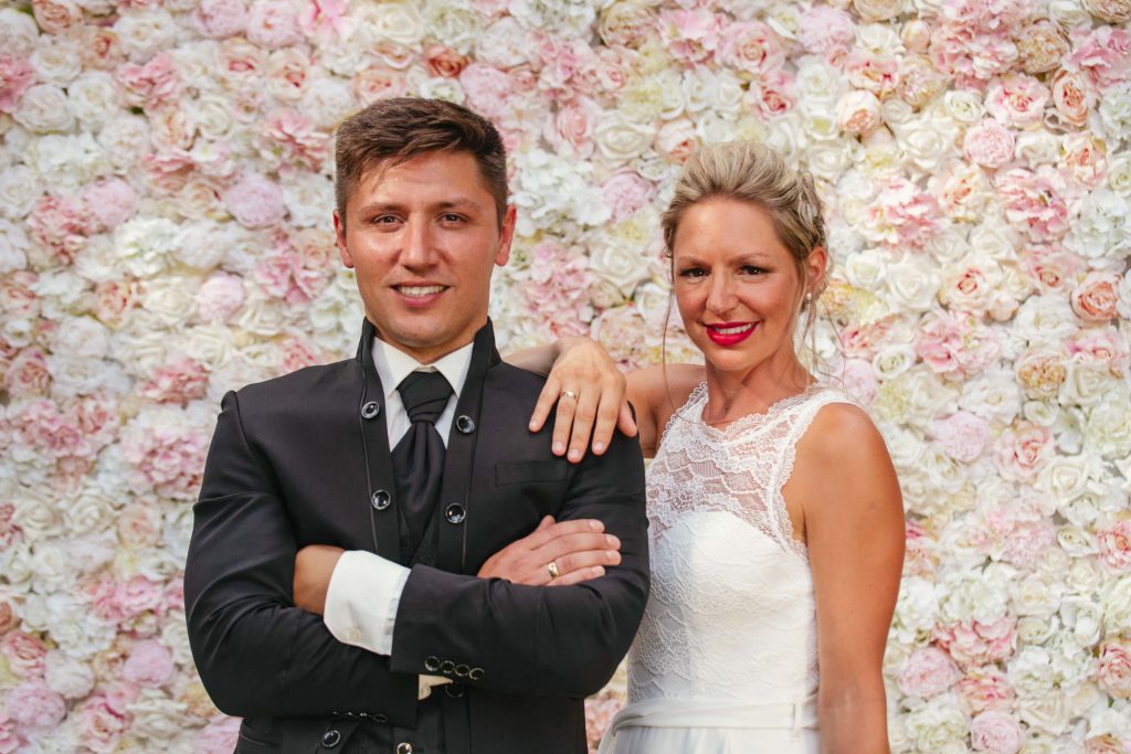 Braut und Bräutigam vor einer Blumenwand aus weißen und rosanen Rosen