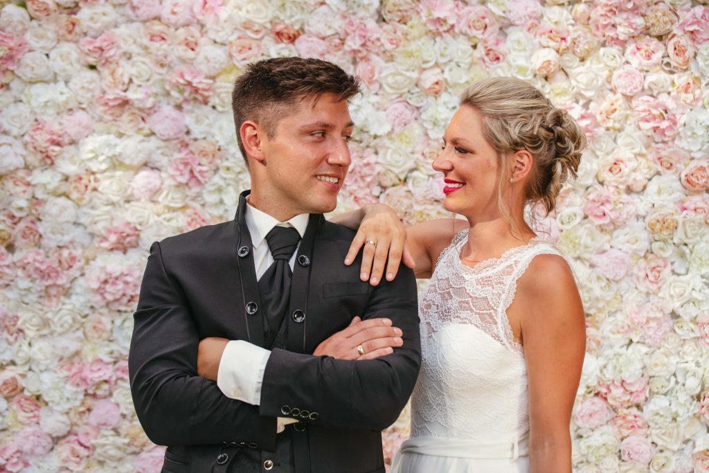 Braut und Bräutigam vor einer Blumenwand aus weißen und rosanen Rosen